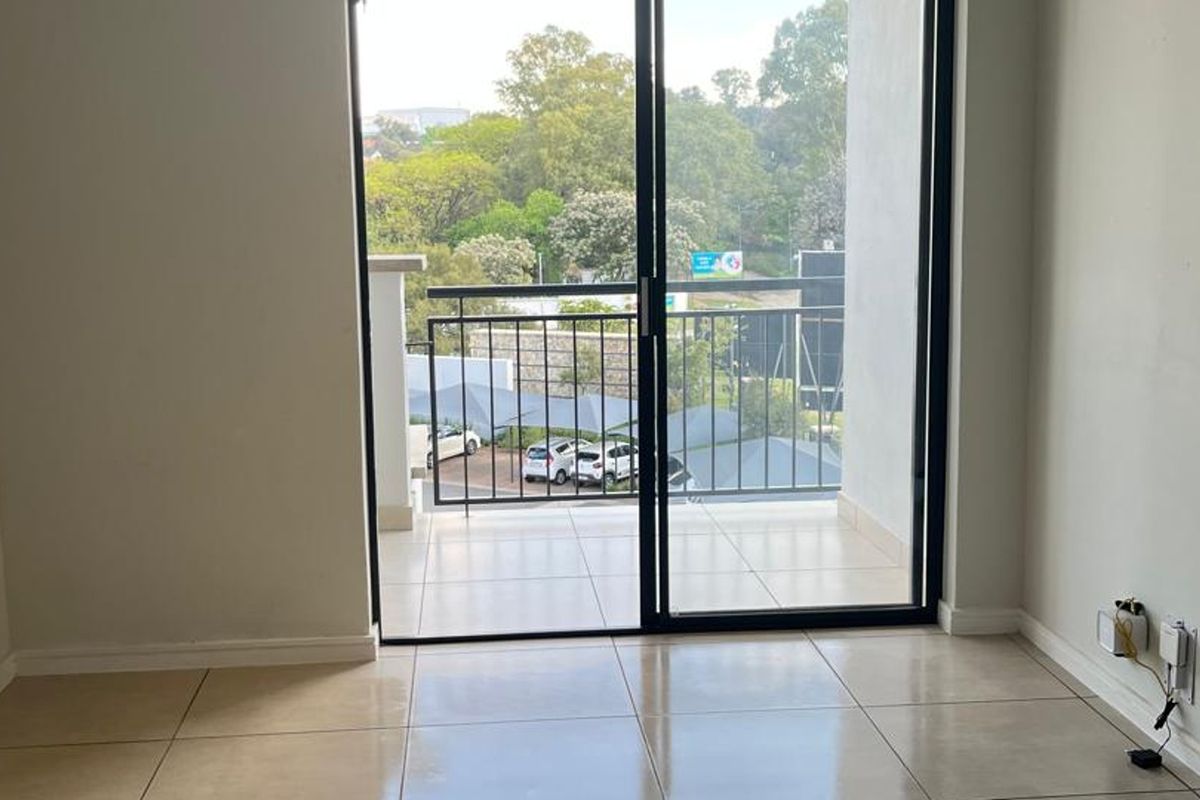 An empty living area featuring large sliding glass doors that open onto a private balcony with tiled flooring.