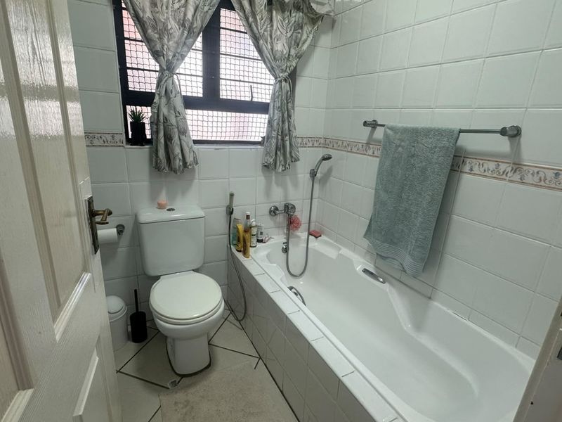 A functional bathroom featuring a built-in bathtub, toilet, and tiled finishes, offering a practical layout with natural light from the window.