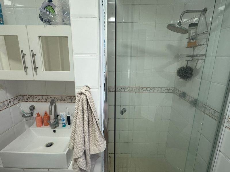Compact bathroom featuring a vessel sink, wall-mounted vanity cabinet, and a glass-enclosed shower with tiled finishes.