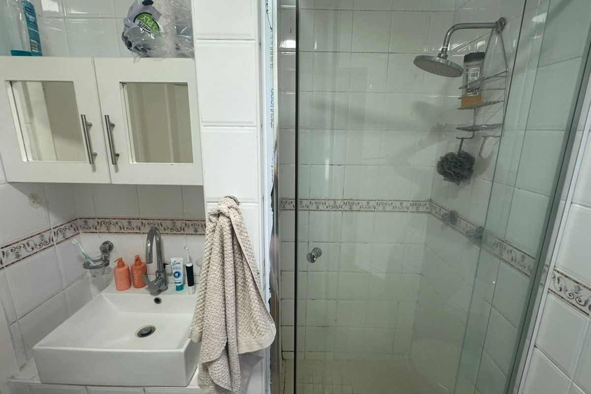 Compact bathroom featuring a vessel sink, wall-mounted vanity cabinet, and a glass-enclosed shower with tiled finishes.