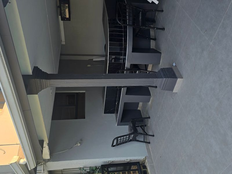 A covered patio area featuring a built-in bar counter, tiled flooring, and structural columns, providing a functional outdoor entertainment space.