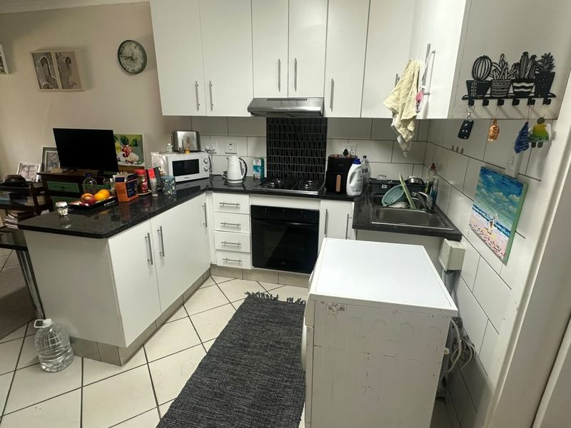 Compact kitchen featuring white cabinetry, granite countertops, built-in oven, gas hob, and tiled backsplash, offering a functional layout for daily use.