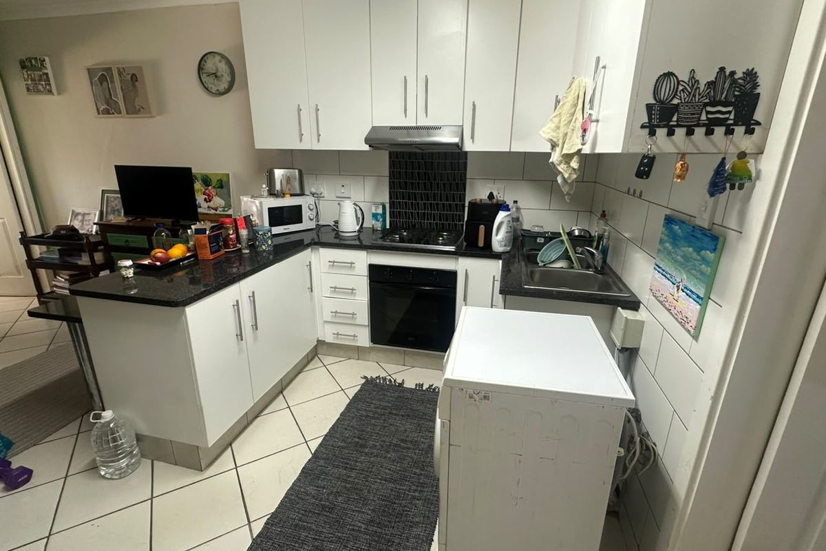 Compact kitchen featuring white cabinetry, granite countertops, built-in oven, gas hob, and tiled backsplash, offering a functional layout for daily use.