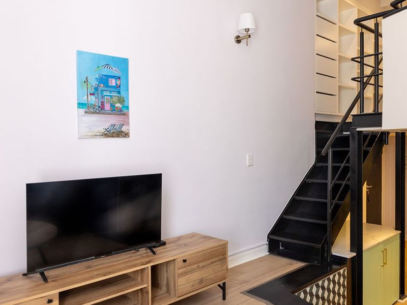 A modern living area featuring a staircase with a metal handrail, built-in shelving, and a wall-mounted light fixture.