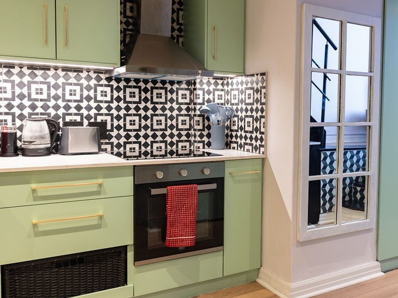 Modern kitchen featuring mint green cabinetry, patterned tile backsplash, integrated appliances, and a built-in oven with extractor fan.