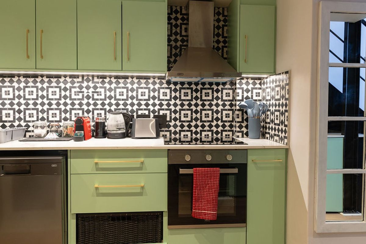 Modern kitchen featuring sage green cabinetry, gold hardware, a striking geometric tile backsplash, stainless steel oven, extractor fan, and integrated dishwasher.