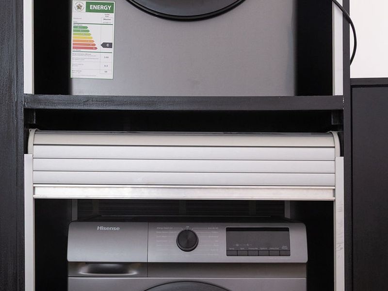 A compact laundry nook featuring built-in cabinetry with a convenient roller shutter door to conceal appliances.