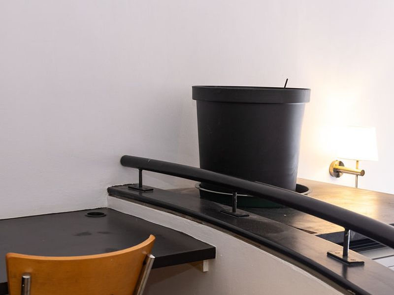 A compact office space featuring a built-in desk, a metal safety railing, and a wall-mounted light fixture.