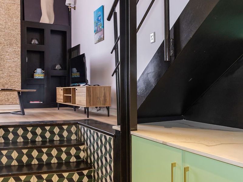 A modern living area featuring a unique tiled staircase, built-in shelving, and custom cabinetry with a stone countertop under the stairs.
