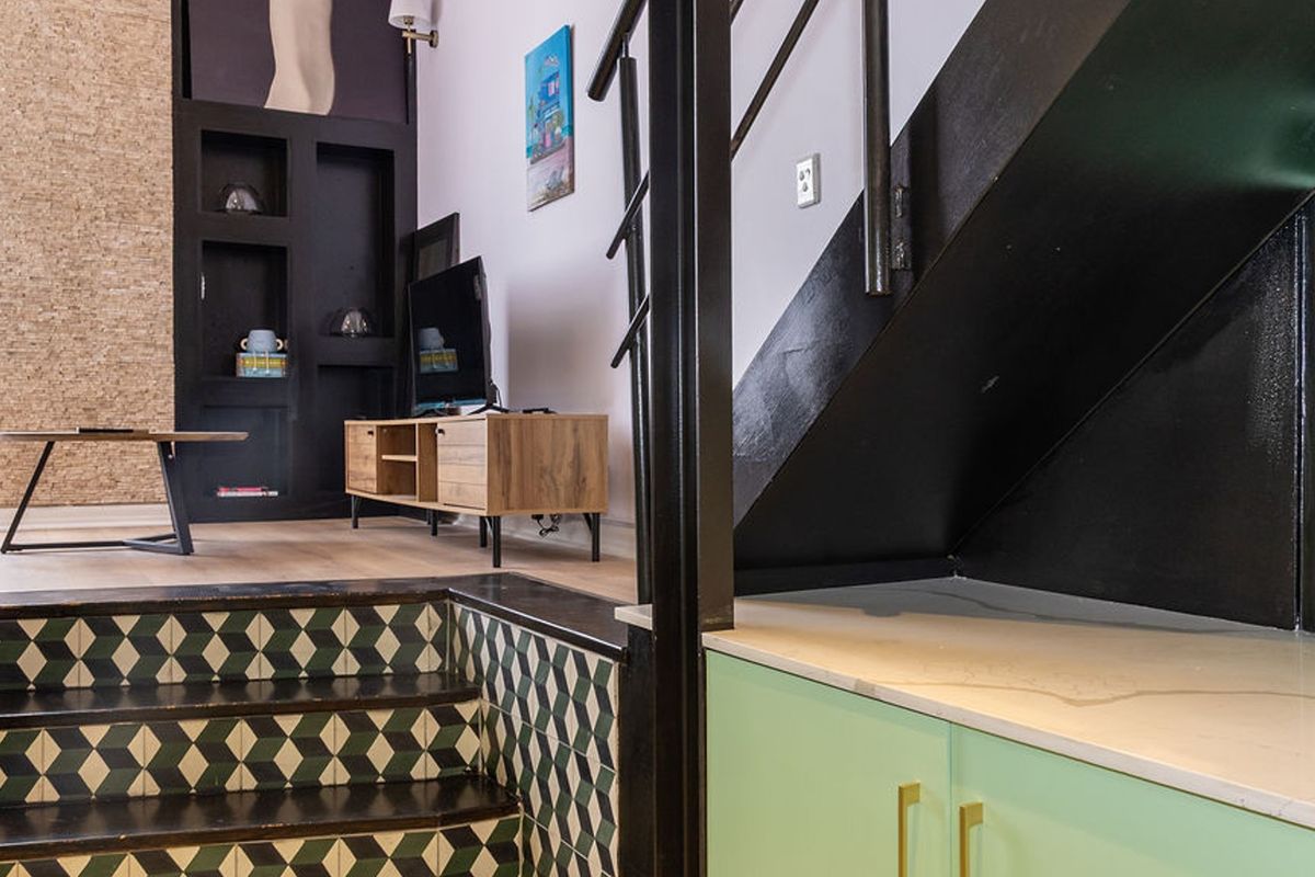A modern living area featuring a unique tiled staircase, built-in shelving, and custom cabinetry with a stone countertop under the stairs.