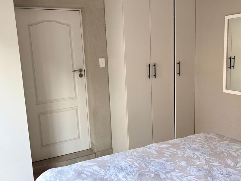 A bedroom featuring neutral-toned built-in cupboards, a standard internal door, and a wall-mounted mirror.