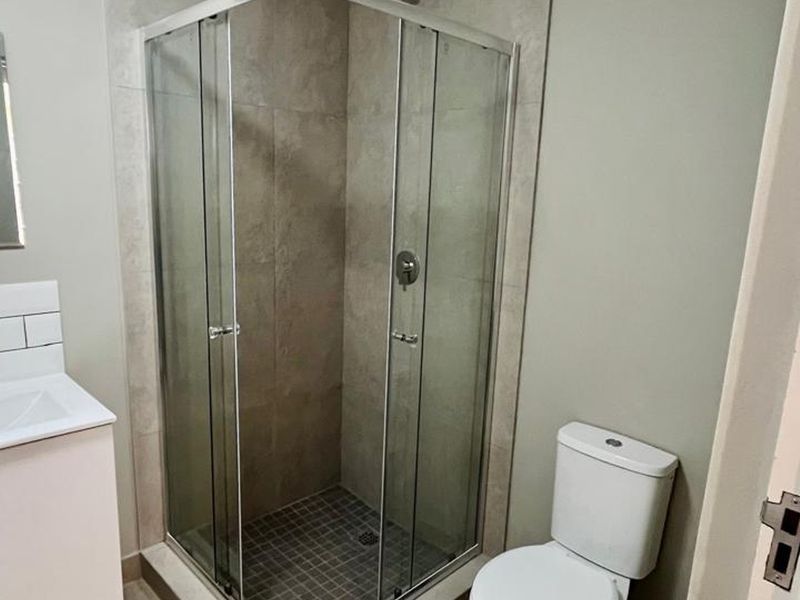 A modern bathroom featuring a glass-enclosed shower, a vanity basin with a mixer tap, and a standard toilet.