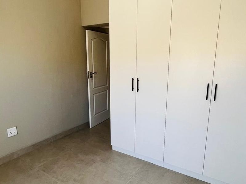 A clean, empty bedroom featuring neutral tiled flooring and modern white built-in cupboards with sleek black handles.