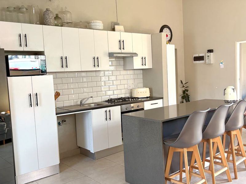 Modern kitchen featuring white cabinetry, subway tile backsplash, stone countertops, and a central island with breakfast bar seating.