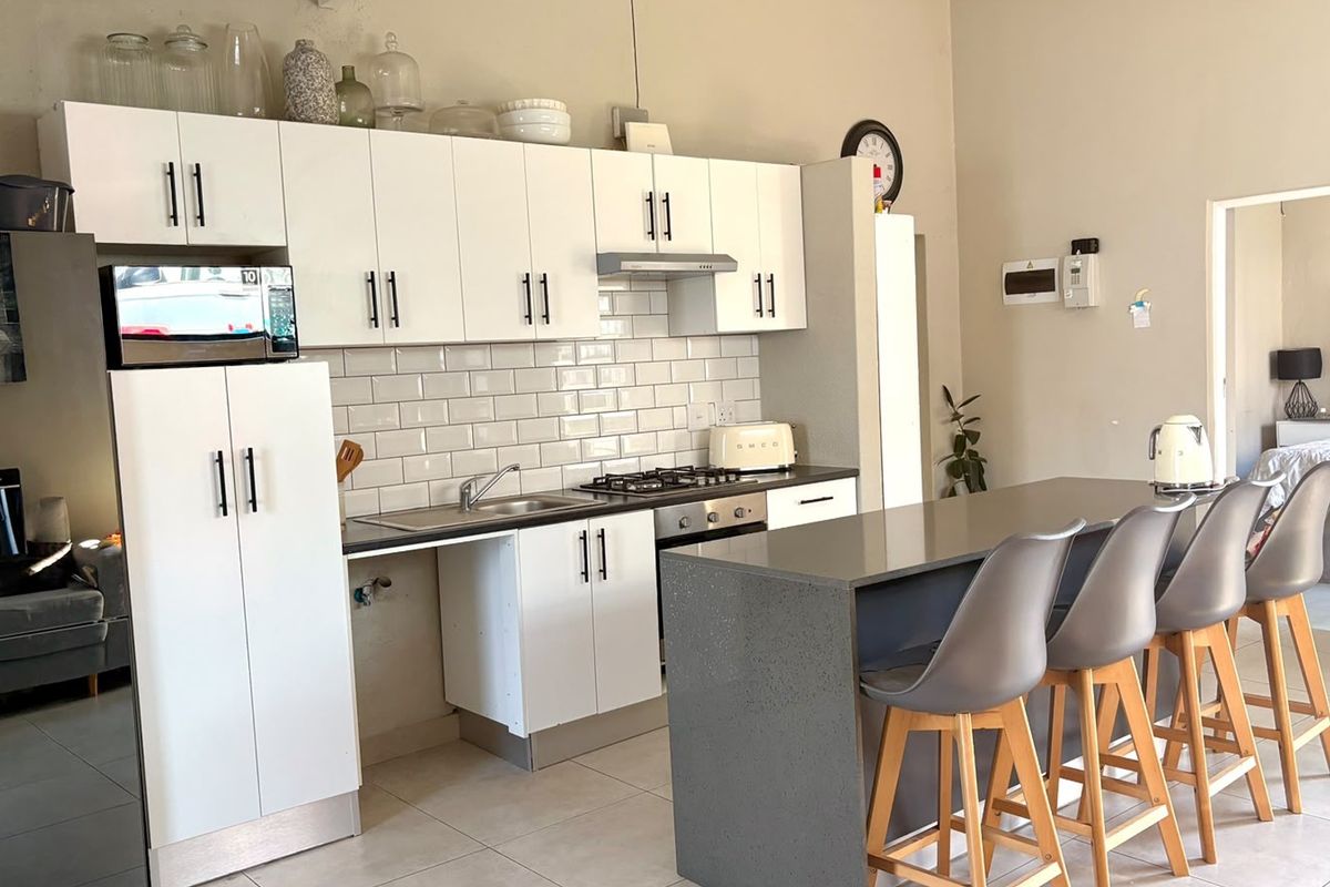 Modern kitchen featuring white cabinetry, subway tile backsplash, stone countertops, and a central island with breakfast bar seating.