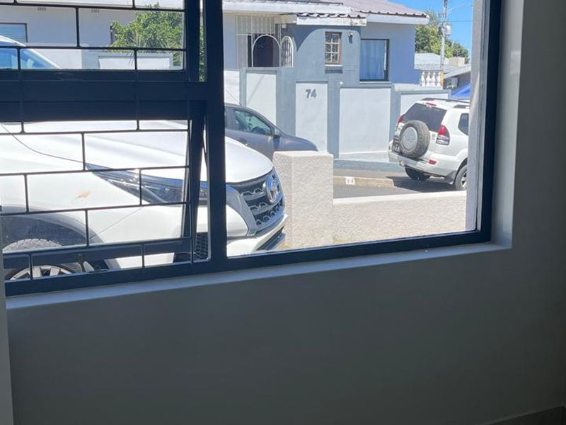 A bright, empty bedroom interior featuring a large window with security bars, offering a view of the street and neighbouring properties.