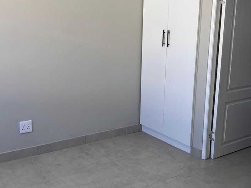 A clean, empty bedroom featuring neutral tiled flooring, a built-in wardrobe, and a doorway leading to an adjacent bathroom.