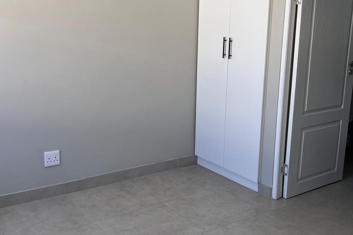 A clean, empty bedroom featuring neutral tiled flooring, a built-in wardrobe, and a doorway leading to an adjacent bathroom.
