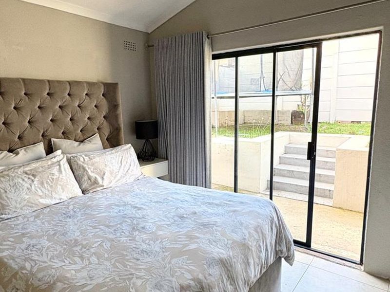 A well-lit bedroom featuring tiled flooring, coved ceilings, and a large sliding glass door providing direct access to the rear patio and garden area.