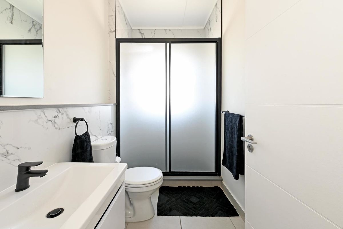 Modern bathroom featuring a vanity basin with black fixtures, a toilet, and a walk-in shower with a frosted glass door and marble-look wall tiling.
