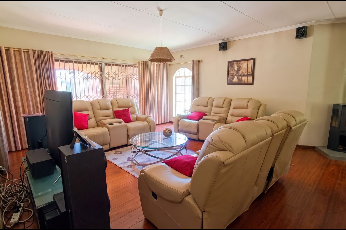 Spacious living room featuring warm wood flooring, a modern freestanding fireplace, and large windows with security gates, offering a comfortable and functional family space.