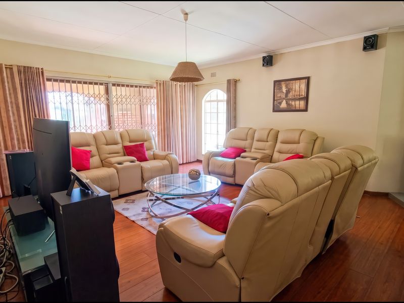 Spacious living room featuring warm wood flooring, a modern freestanding fireplace, and large windows with security gates, offering a comfortable and functional family space.