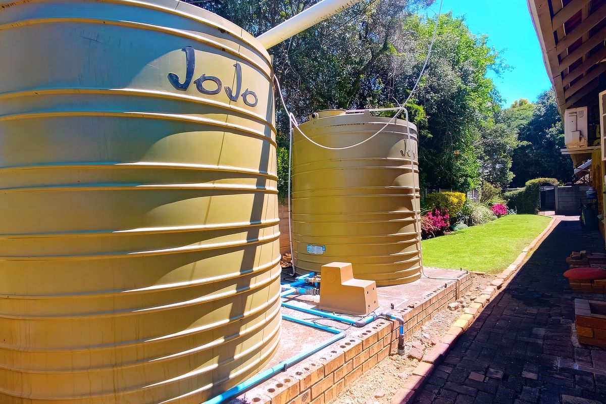 Rear exterior area featuring two large water storage tanks, brick paving, and a functional water filtration system alongside a landscaped garden.