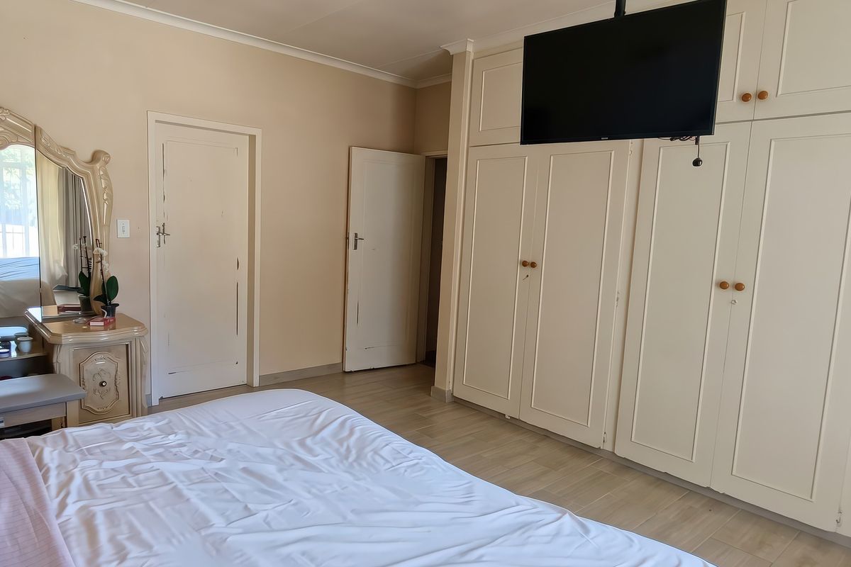 A bedroom featuring extensive built-in floor-to-ceiling cupboards, laminate flooring, and neutral wall tones, offering ample storage space.