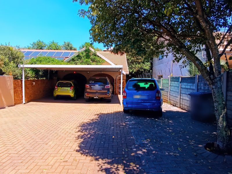 Front exterior view featuring a paved driveway, covered carport, boundary wall, and solar panels installed on the roof.