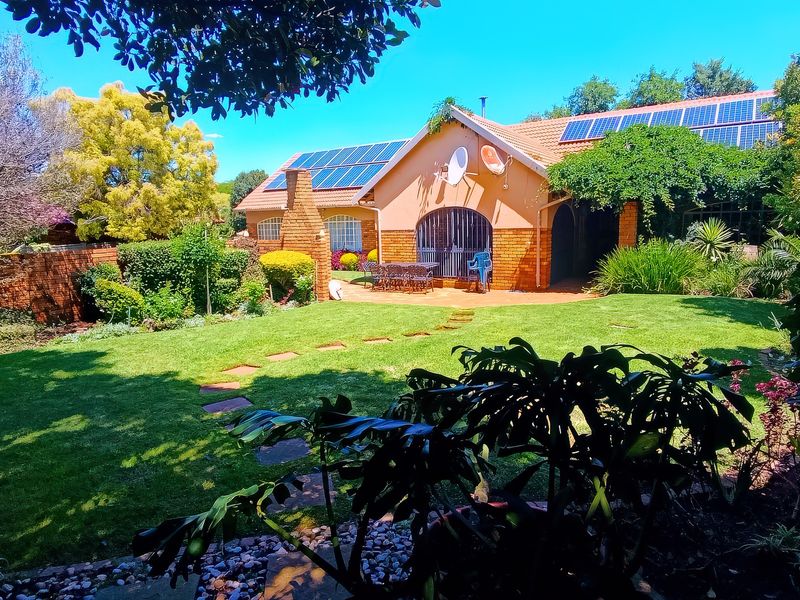 A well-maintained rear garden featuring a spacious lawn, paved pathway, and a brick-faced house exterior equipped with roof-mounted solar panels.