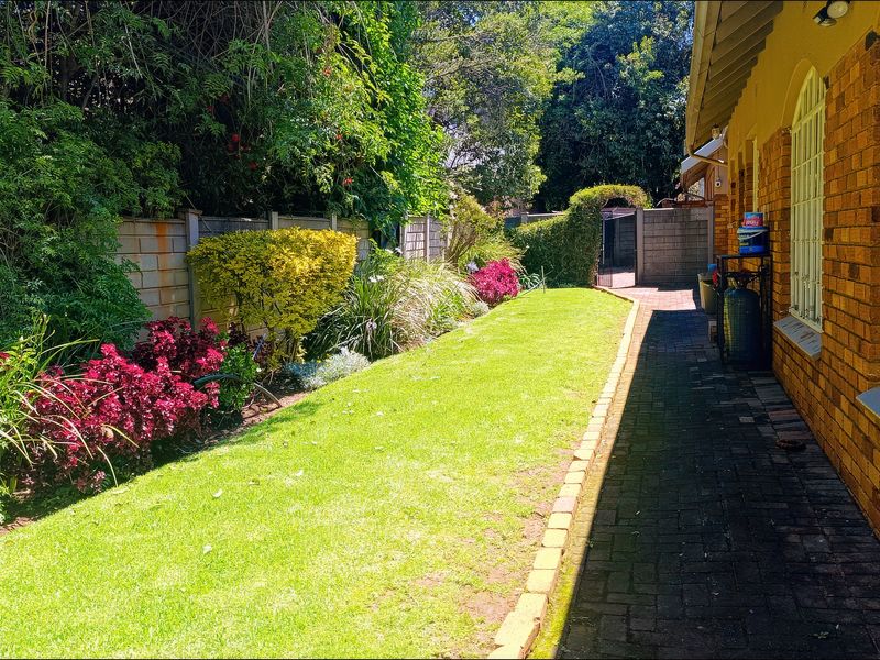 A well-maintained rear garden featuring a brick facade, a paved walkway, and established landscaping along the boundary wall.