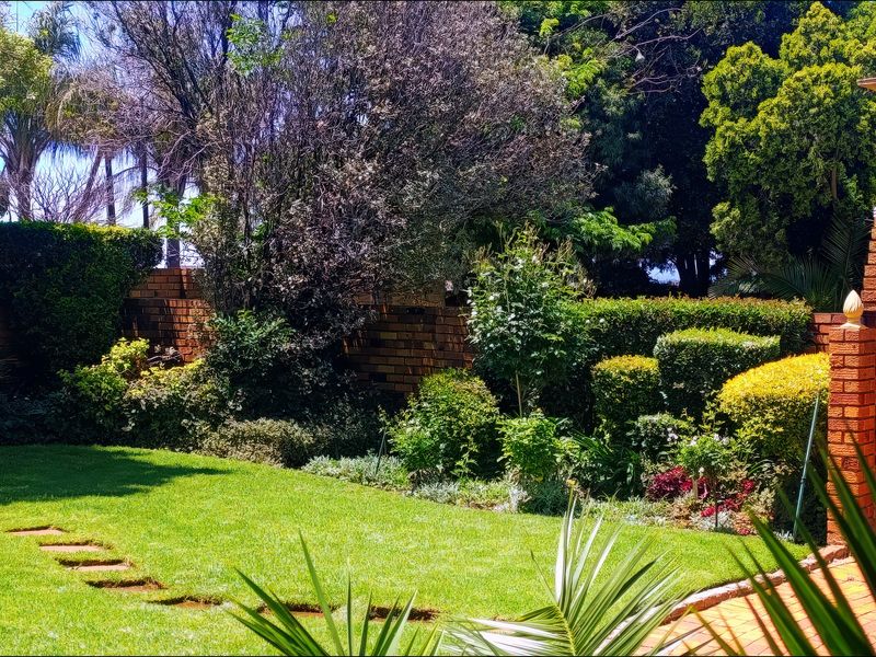 A well-maintained garden featuring a lush lawn, mature landscaping, brick boundary walls, and a built-in brick fireplace perfect for outdoor entertaining.