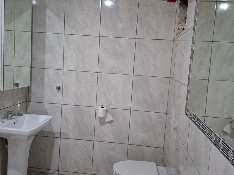 A functional bathroom featuring full-height wall tiling, a pedestal basin, and a wall-mounted mirror.