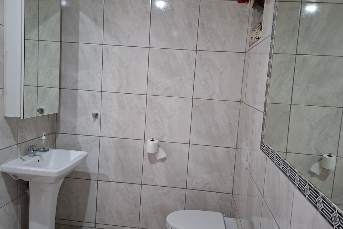 A functional bathroom featuring full-height wall tiling, a pedestal basin, and a wall-mounted mirror.