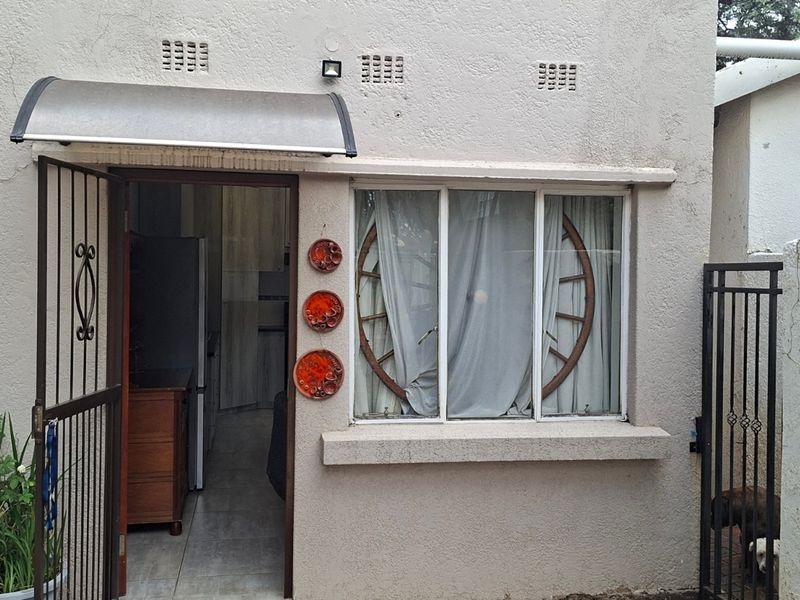 Front entrance of the cottage featuring a security gate, protective awning, and a window with a view into the interior living space.