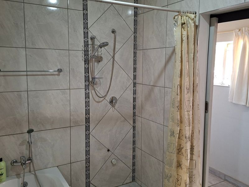A functional bathroom featuring tiled walls, a combined bathtub and shower setup, and a wall-mounted towel rail.