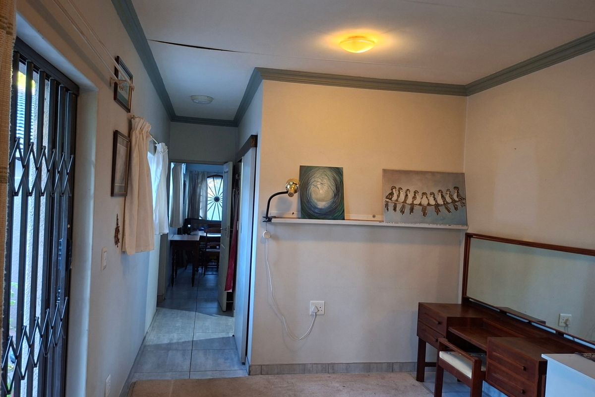 A living area featuring tiled flooring, ceiling cornicing, and a security gate, with a visible crack in the ceiling requiring attention.