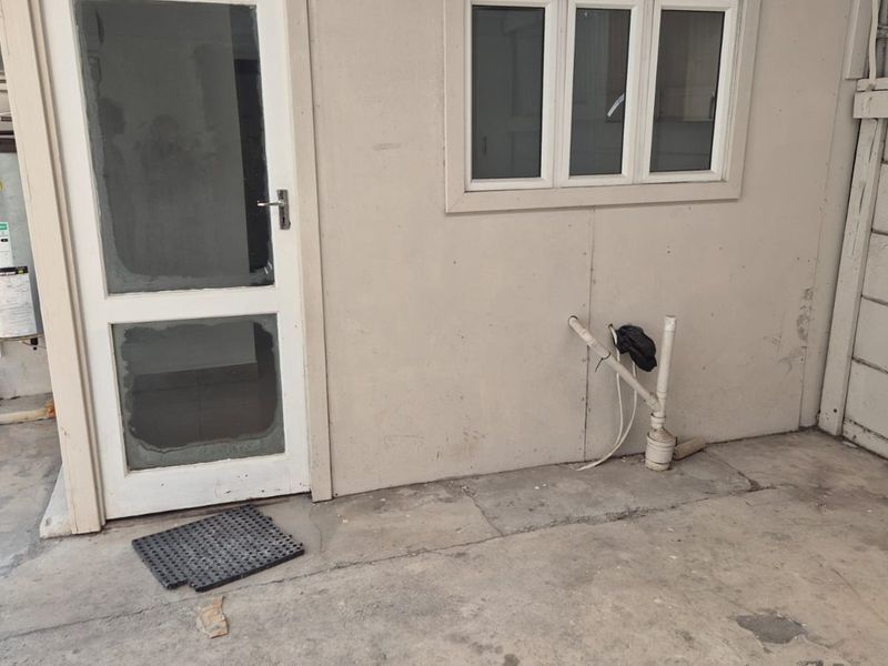 An outdoor utility area featuring an electric geyser, exposed plumbing connections, and concrete flooring, providing functional space for laundry or maintenance equipment.