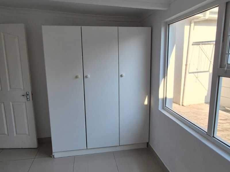 A bedroom featuring tiled flooring, built-in cupboards, and large windows with security bars, offering a functional and well-lit living space.