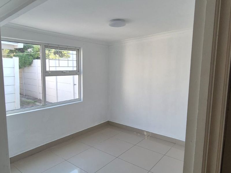 A clean, empty bedroom featuring neutral tiled flooring, white walls, and an aluminium-framed window with security bars.