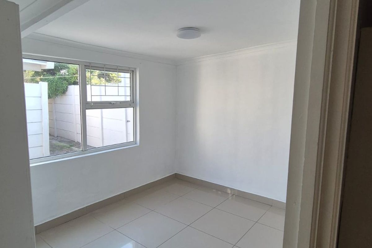 A clean, empty bedroom featuring neutral tiled flooring, white walls, and an aluminium-framed window with security bars.