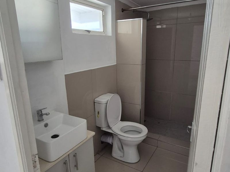 A clean, functional bathroom featuring a modern vanity, toilet, and a tiled shower enclosure with neutral finishes.