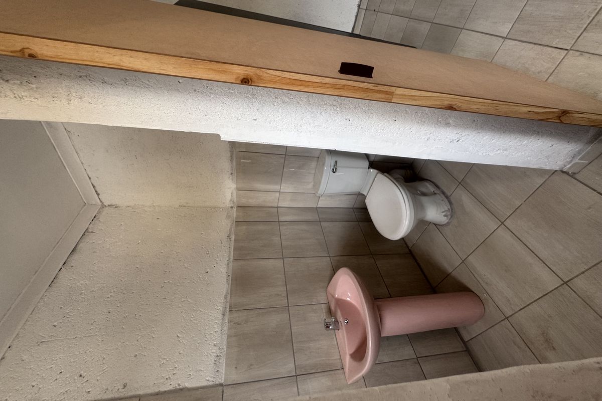 A compact bathroom featuring a pedestal basin and toilet, finished with neutral floor tiles and partially tiled walls.