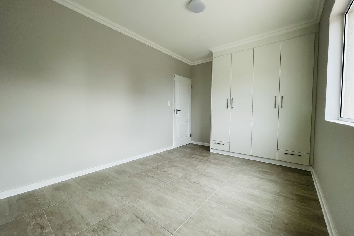 A bright, empty bedroom featuring neutral tiled flooring, built-in wardrobes, and clean, modern finishes.