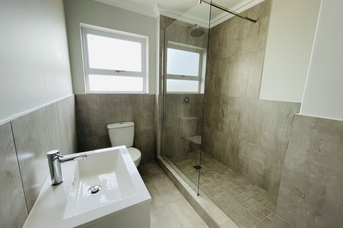 Modern bathroom featuring a walk-in shower with glass enclosure, contemporary vanity basin, and neutral floor-to-ceiling tiling.