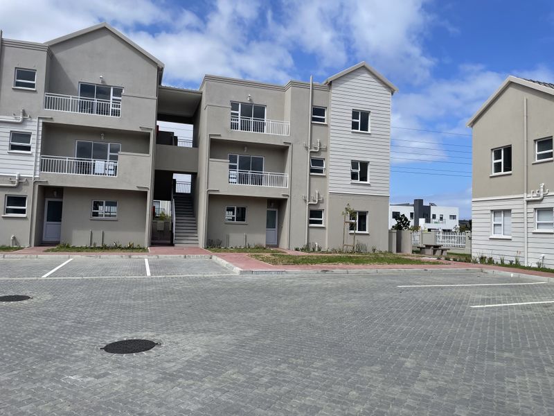 Exterior view of a modern apartment complex featuring paved parking, balconies with railings, and a communal staircase.