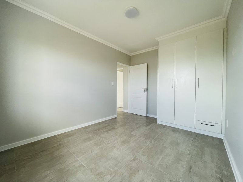 A clean, neutral bedroom featuring large-format floor tiles, built-in white cabinetry, and crown molding, offering a bright and versatile living space.