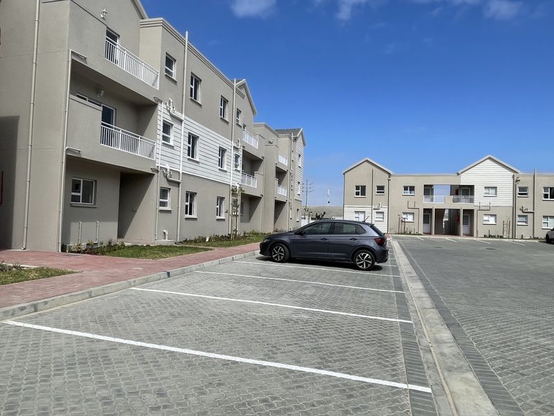 Exterior view of a modern apartment complex featuring paved parking bays, multi-story residential blocks with balconies, and well-maintained building facades.