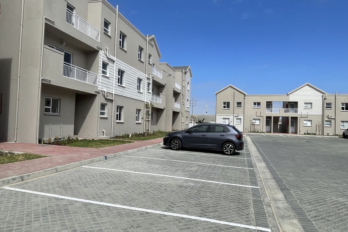 Exterior view of a modern apartment complex featuring paved parking bays, multi-story residential blocks with balconies, and well-maintained building facades.