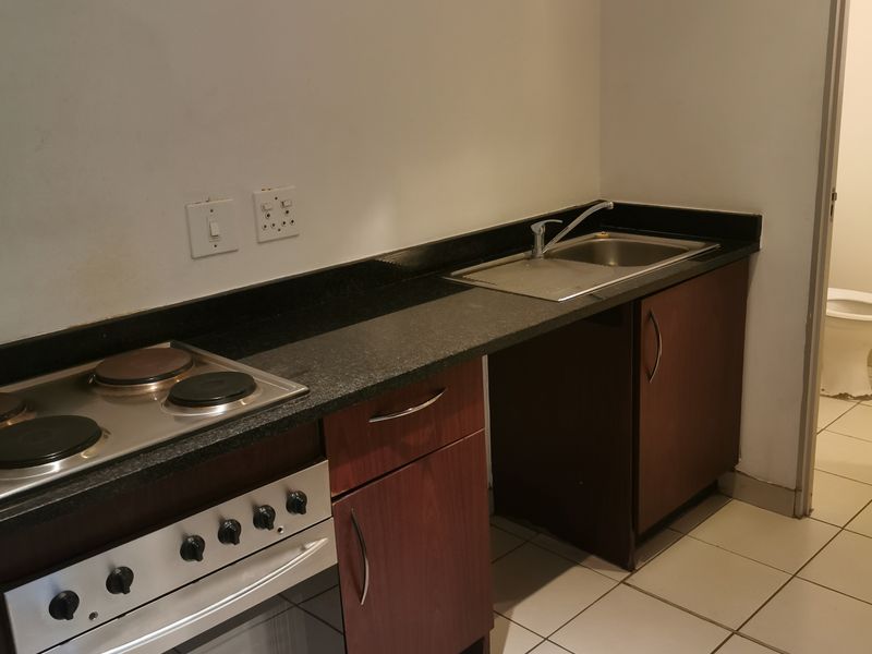 A compact kitchen featuring a built-in oven, electric hob, granite countertops, and tiled flooring, requiring minor cosmetic updates.